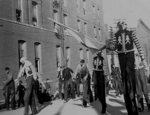 View of men on stilts in various dress walking along unidentified parade route during the Priests of Pallas parade.